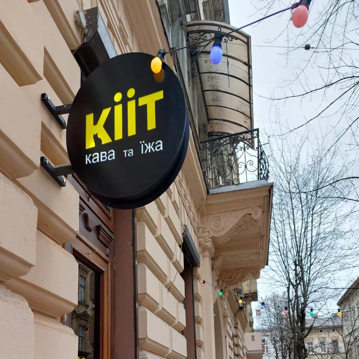 Кругла торцева вивіска-кронштейн KiiT кава та їжа, закріплена перпендикулярно до фасаду