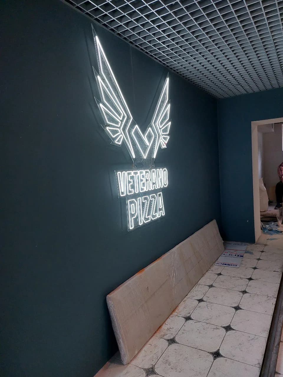 Неонова вивіска Veterano Pizza з крилами на темній стіні піцерії